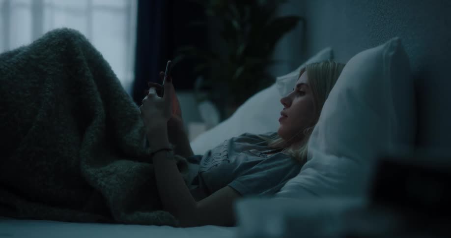 A woman is laying down and texting in her bed