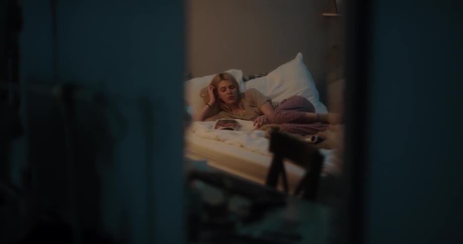 Young white woman lying down in bed at her bedroom and reading a magazine