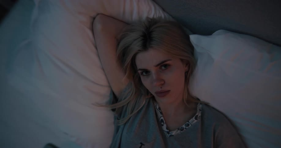 Blond teenager lays on the pillows in bed with her right hand behind her head