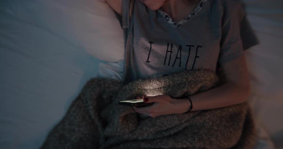 A young woman checks her phone while lying in bed before resting the phone on her chest