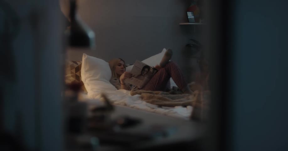 Young white woman lying in her bed at her bedroom reading a magazine