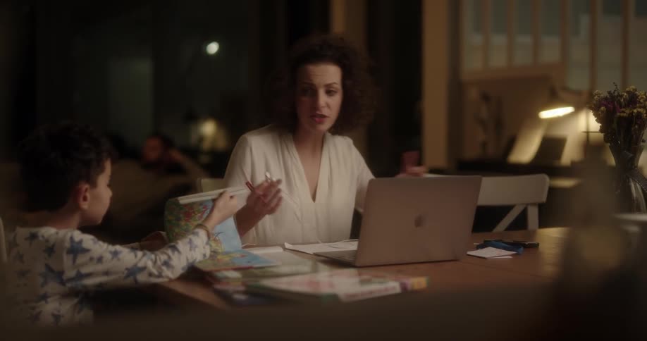Woman scolds her young son then puts earphones in her ears and looks at her laptop smiling and laughing