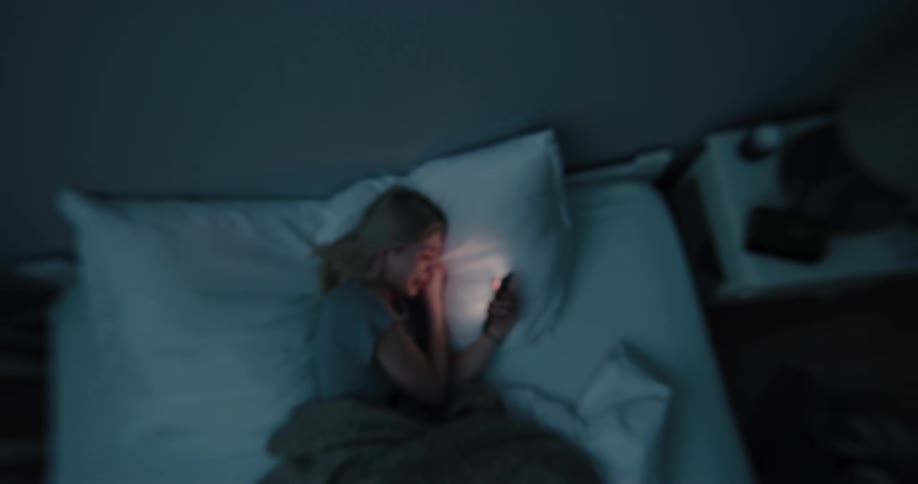 A woman cries as she uses her cell phone in bed