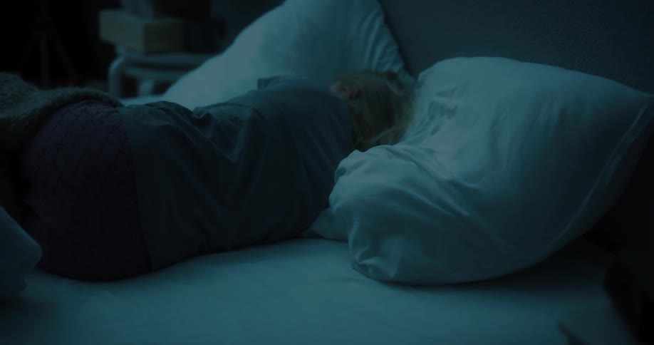 A woman tosses and turns while sleeping in a bed in a dark bedroom