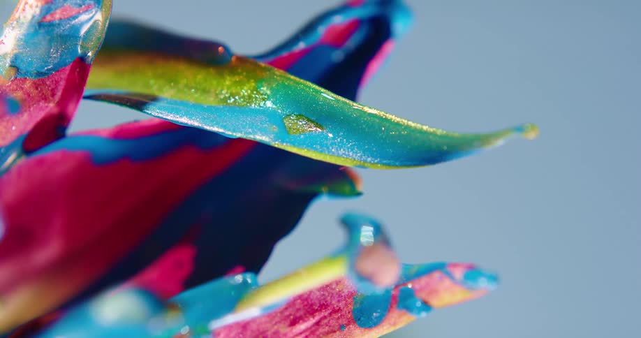Colorful rainbow liquid glitter shimmering ink drips sideways from a flower