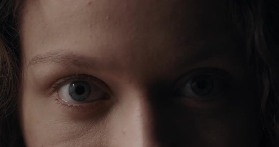 Close up of the eyes of a woman looking at the camera inside a dimly lit room