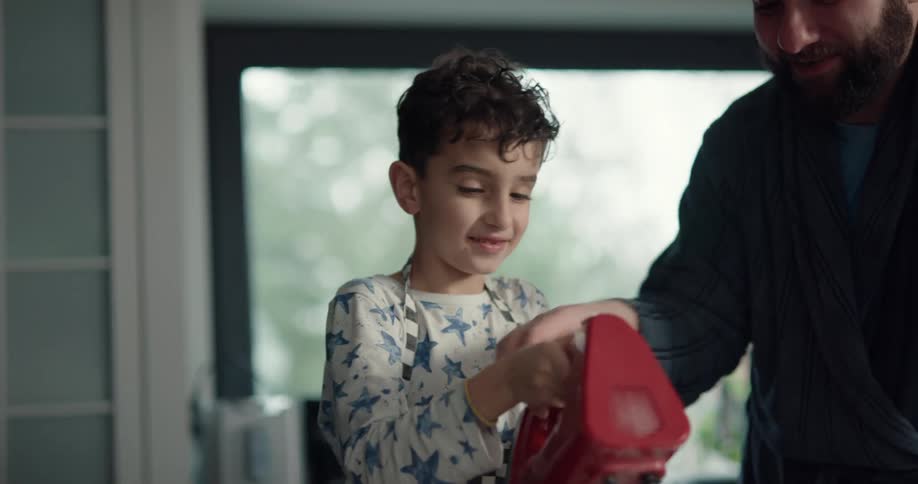 Father teaching his son how to use a hand mixer in the kitchen at home