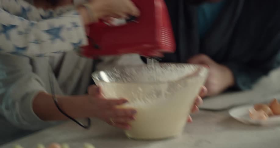 Husband kisses his wife and then they laugh as they watch their son mix some batter with an electric mixer