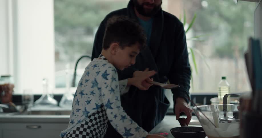 Father teaching his son how to cook pancakes in the kitchen at home