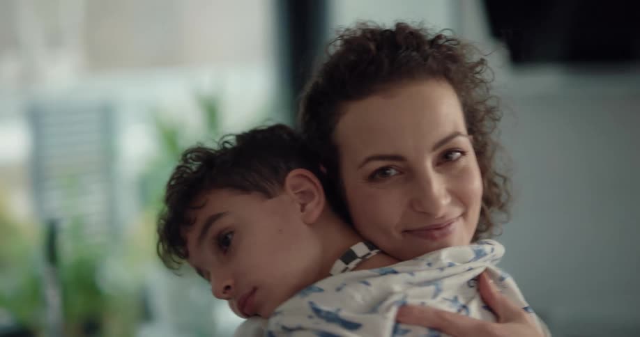 A woman smiles into the camera while hugging a young boy