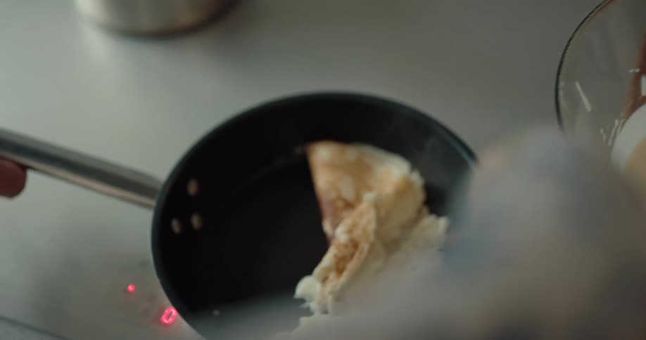 A boy struggles to flip a pancake as his mom tries to help