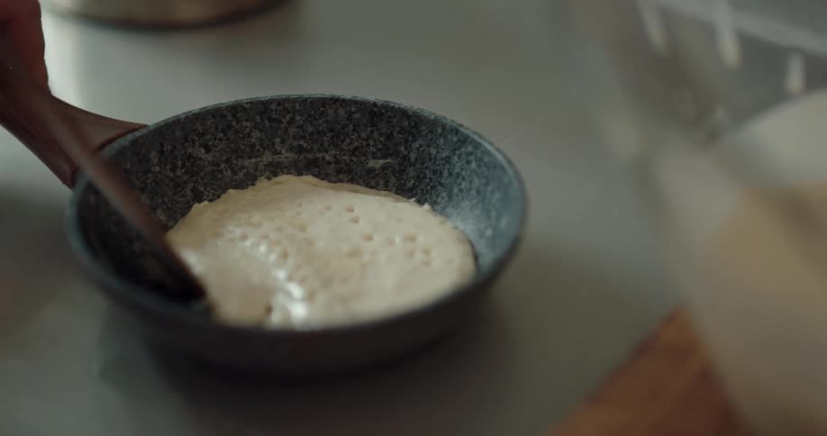 A mother is helping her daughter learn to cook pancakes in the kitchen in the morning