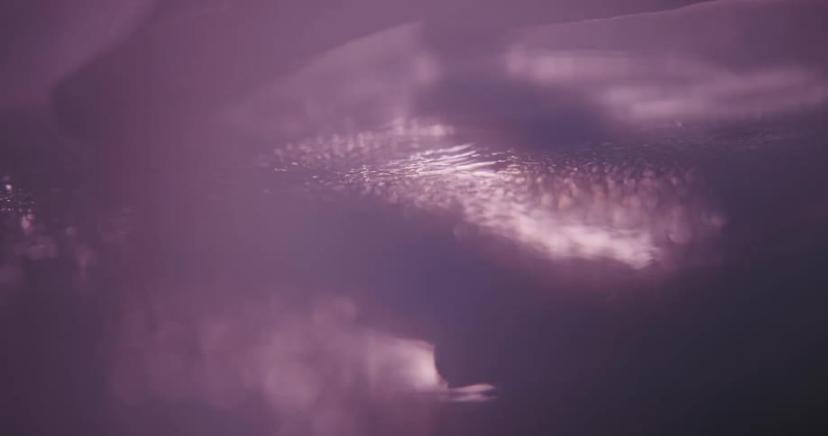 Fingers touch a wet shimmering surface leaving behind ridges and lines