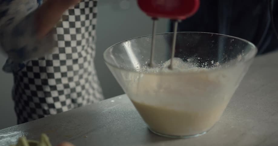 A boy helps his mother use a hand mixer to blend batter