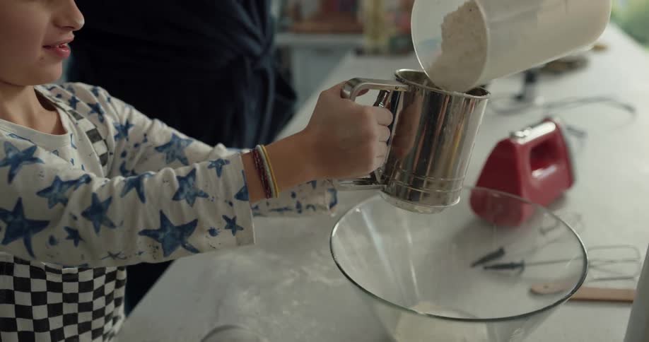 Dad kisses his son on the head as they sift flour to make breakfast together