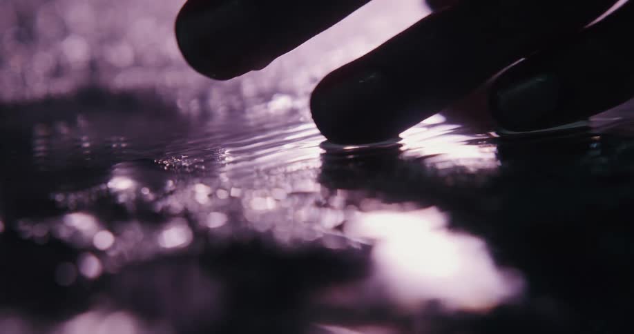 A person runs their fingers through water as rain falls