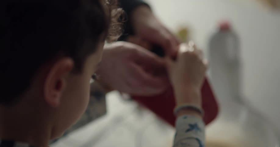 An adult helps a boy to mix batter in a mixing bowl using a handheld mixer