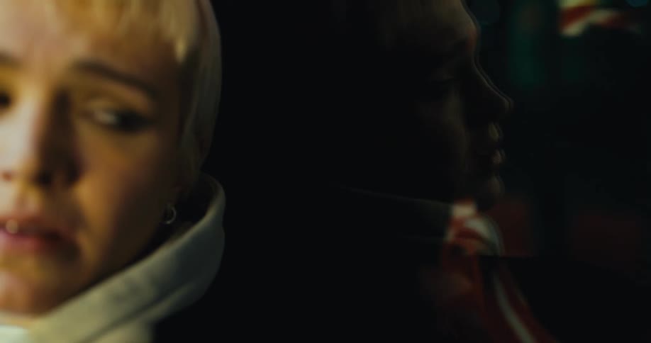 A woman looks around in fear and closes her eyes while standing against a window