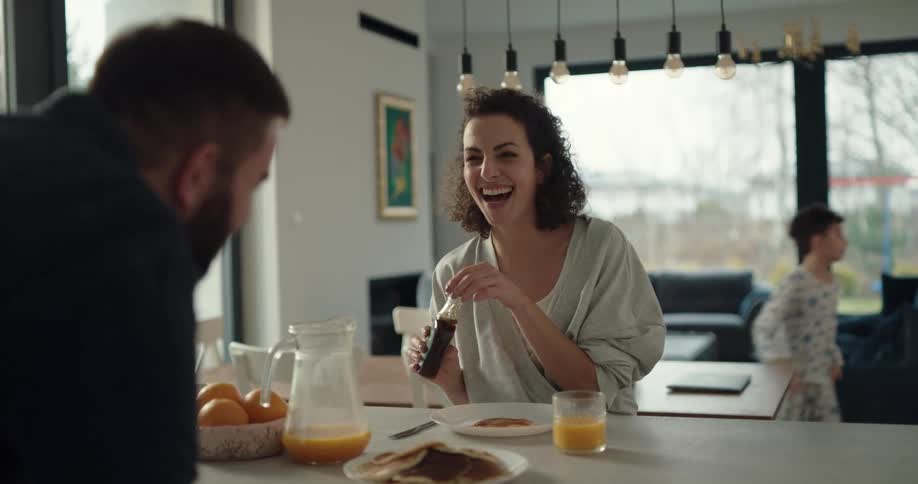 A woman laughs as she pours syrup over her pancakes