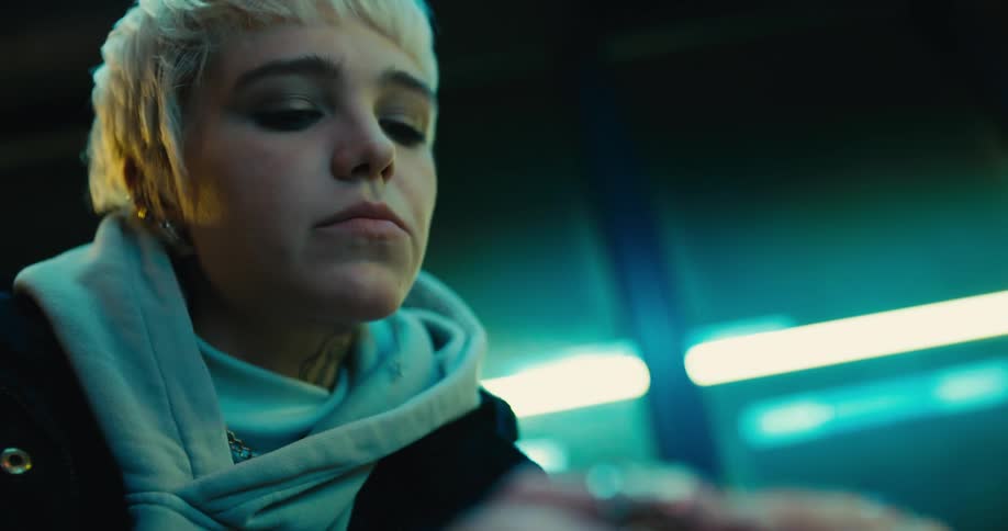 Woman wearing hoodie sits fidgeting under fluorescent lights