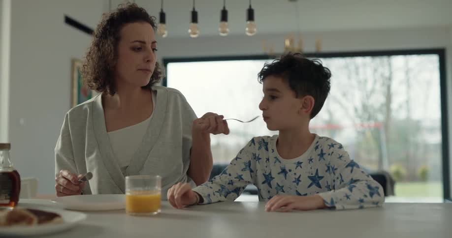 Woman cuts a piece of pancake and feeds it to her son as her husband watches and they all laugh