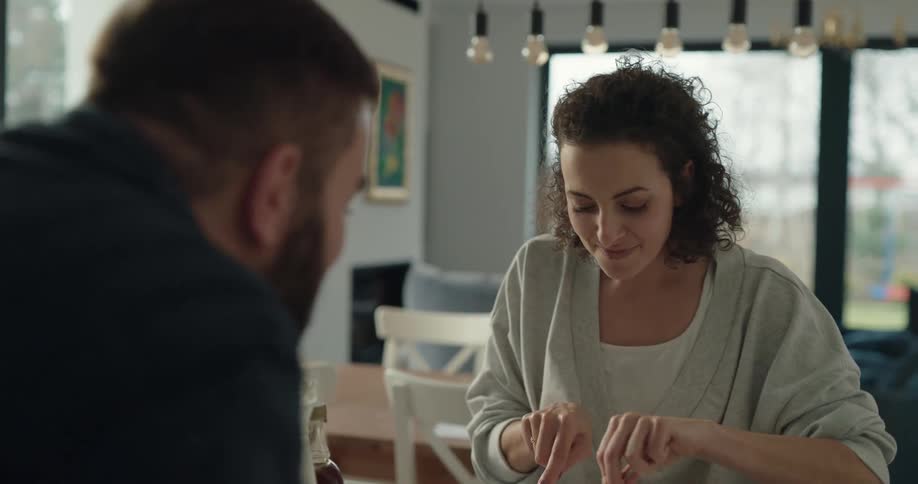 A woman is enjoying a meal while also feeding some of it to a man while they sit at a table in a home during the daytime