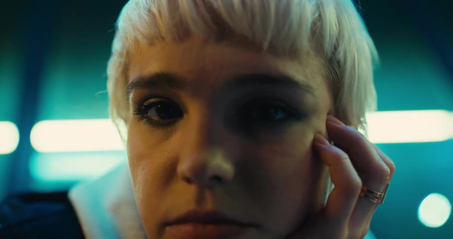 A young woman poses with her head resting in her hand in a dark room