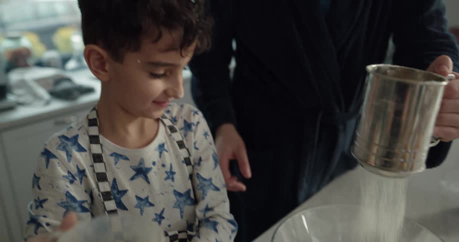 Father and son sifting flour over a bowl in the kitchen at home