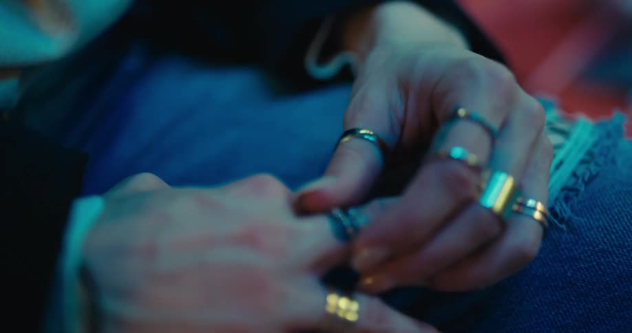 A woman sitting fidgeting with her rings with city lights visible through the window behind her