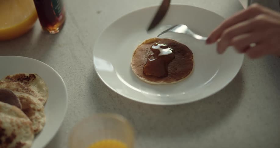 A woman serves herself a pancake and her husband adds syrup she smiles while eating