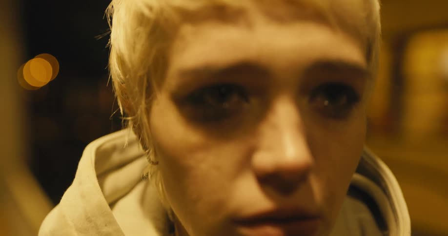 Young white woman with a sad looking face wearing a hoodie and jacket standing outdoors and smoking a cigarette