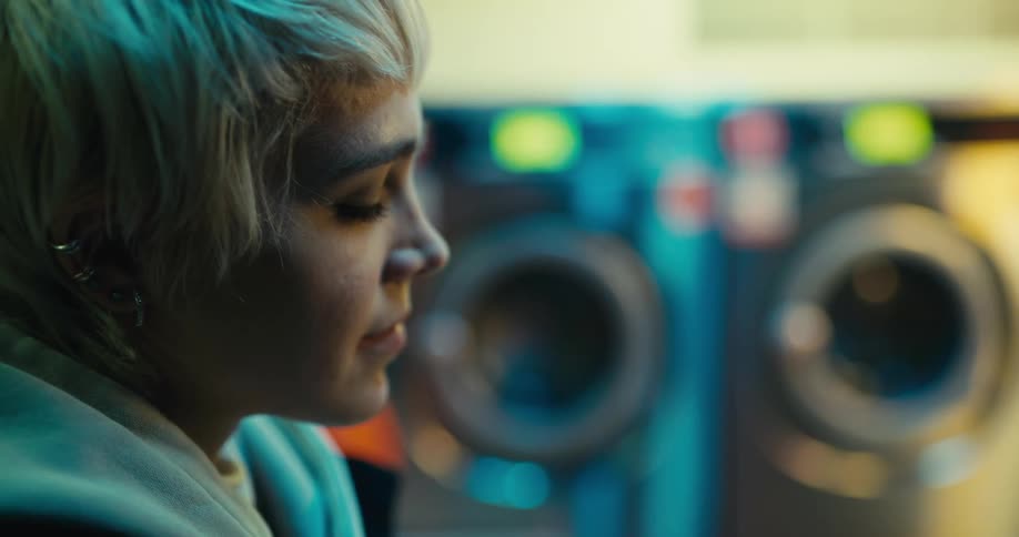 Blond teenaged girl sits thoughtfully then begins to write in a lined notebook while at the laundromat