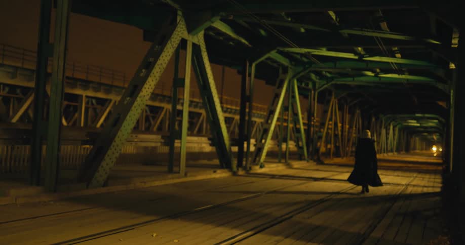 A woman wearing a long coat is walking along an urban railway at night