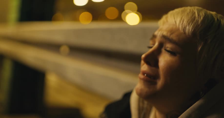 A woman sobs as she leans against a bridge and traffic passes by