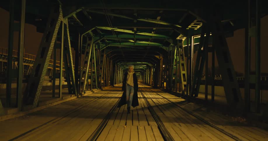 A woman is walking on a bridge in a city at night
