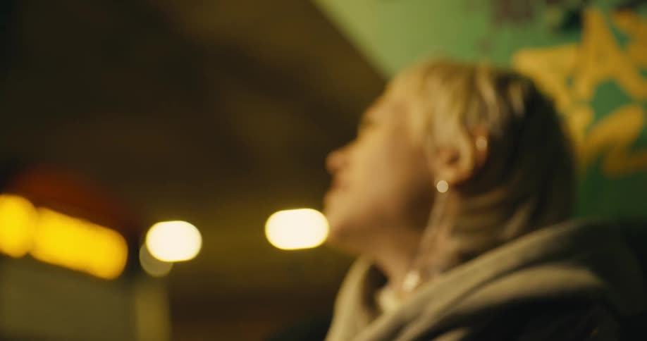 Young blonde woman screaming at the phone slides down crying on the street at night