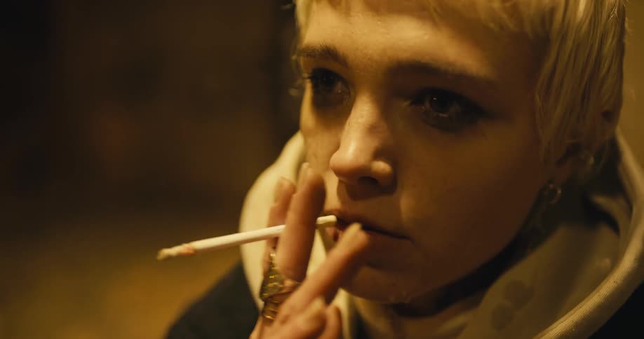 A teenage girl with tears streaming down her face smokes outside on a cold night
