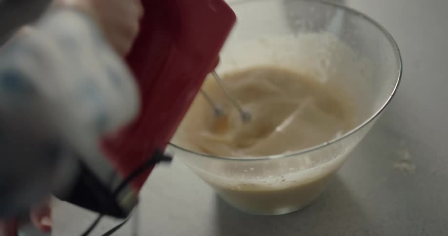 A young boy mixes batter in a kitchen and talks to his dad who is standing next to him helping