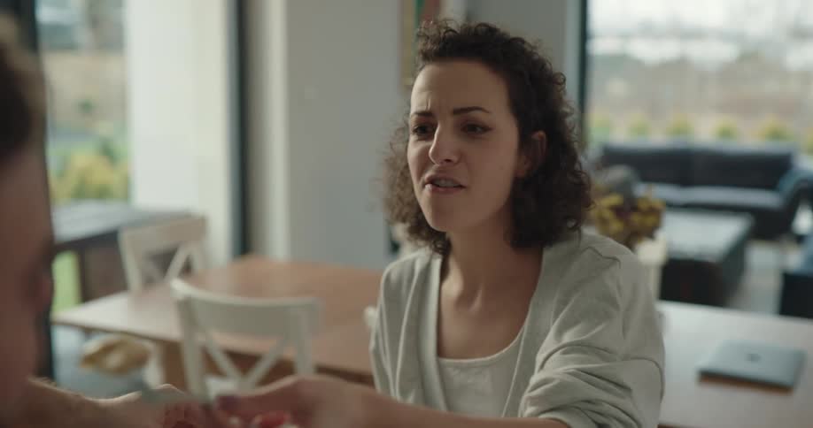 A woman feeds a man sitting across from her a piece of her pancake while sitting at a dining table in house during the day