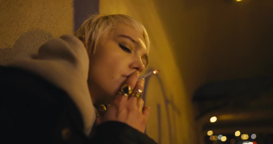 A woman is standing outdoors in a city and smoking