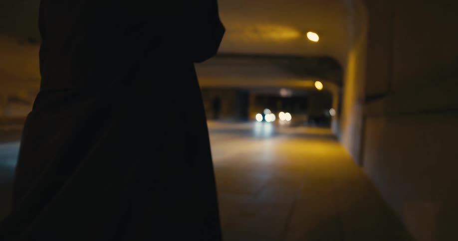 A teenage girl walks through a tunnel and turns in a circle looking around her as she smokes and cars drive past