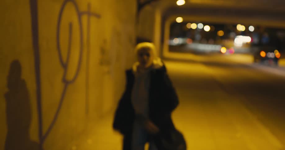 Man steals the purse of a young woman walking under a bridge in the city at night