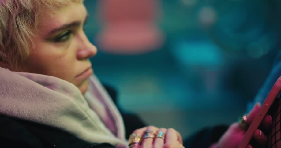 A woman sits fidgeting and texting looking around in an unsettled manner
