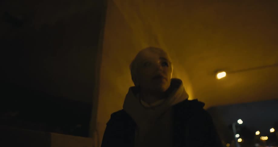 A person walks beneath an overpass in a city while smoking a cigarette at night