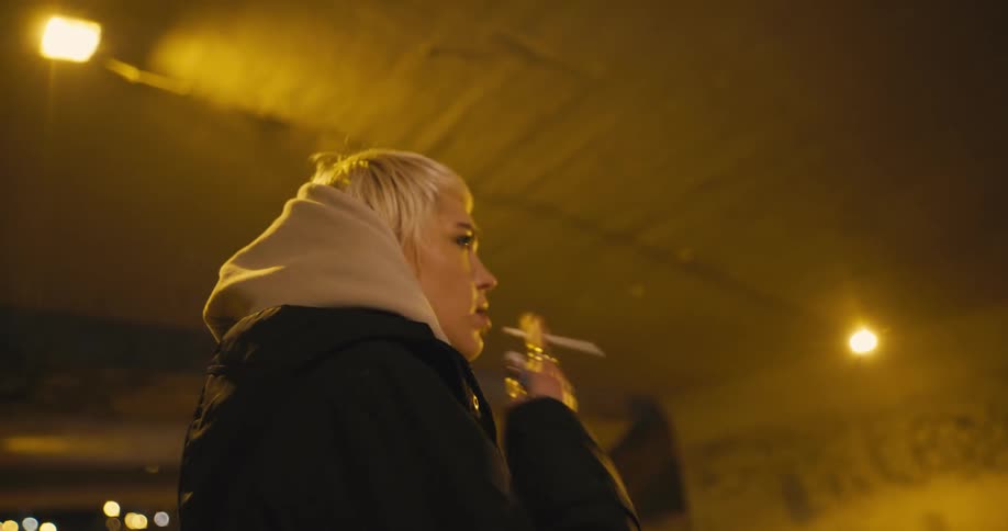 A woman is standing outdoors at night and is smoking