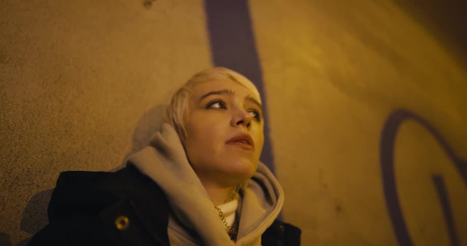 A woman smokes a cigarette against a graffitied wall