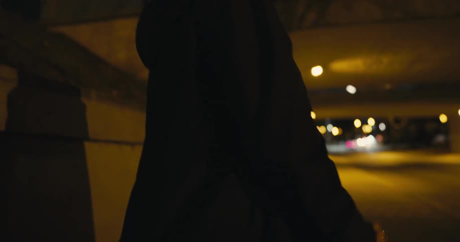 A woman smokes a cigarette while walking through a tunnel at night
