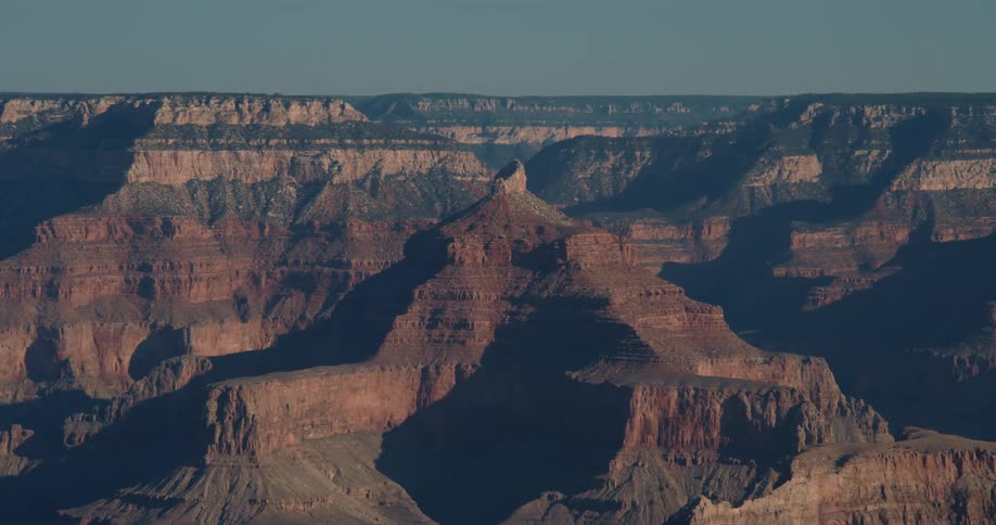 The sun shines brightly upon rock formations and mountains under a clear sky