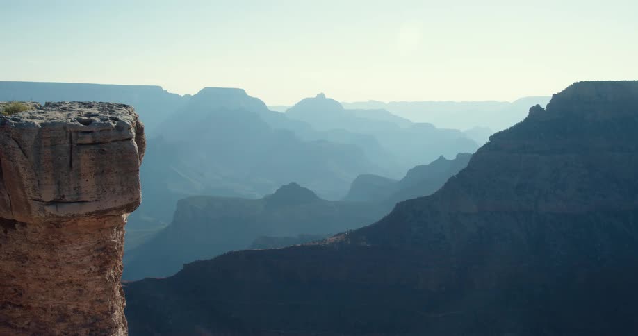 A ledge overlooks silhouettes of mountains in a hazy sky