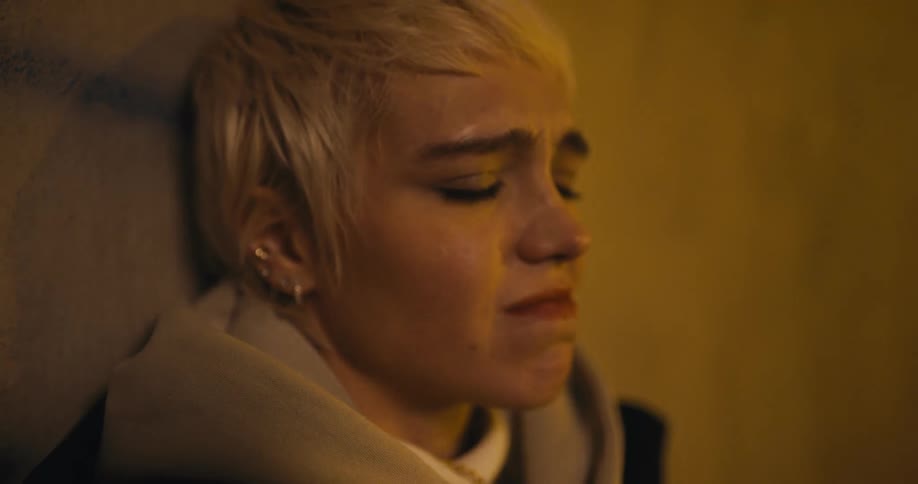 Woman sits near concrete wall frowning and tearing up